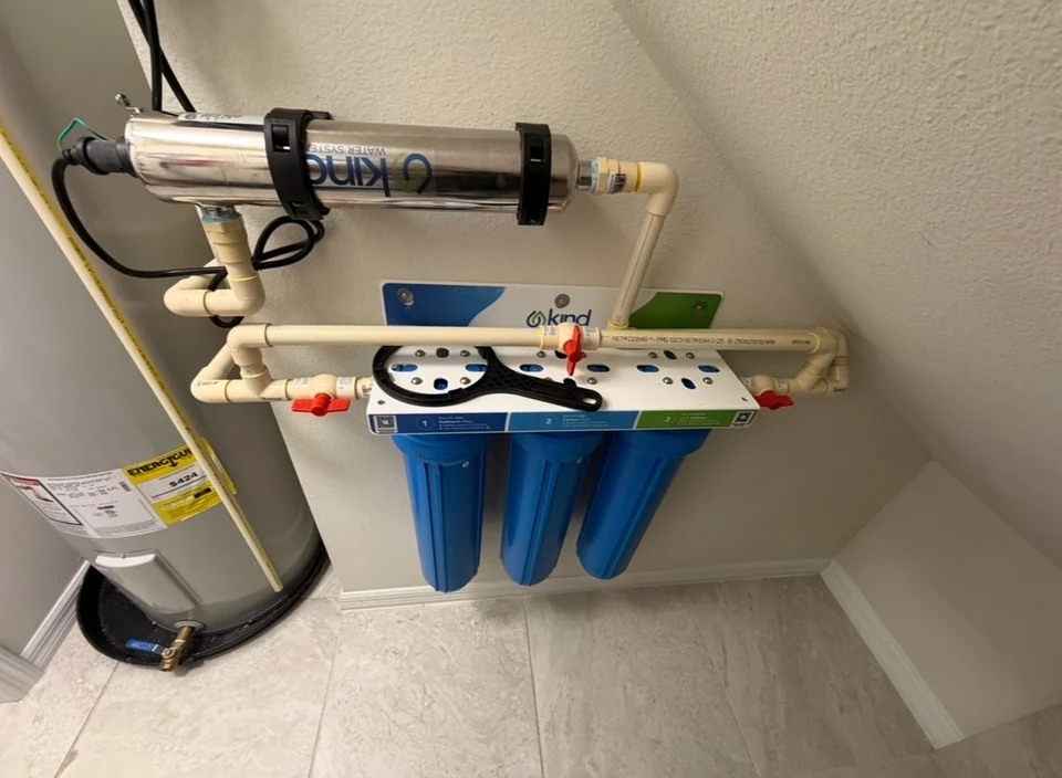 A three-housing water filtration system with an additional stainless-steel treatment unit beside a water heater.