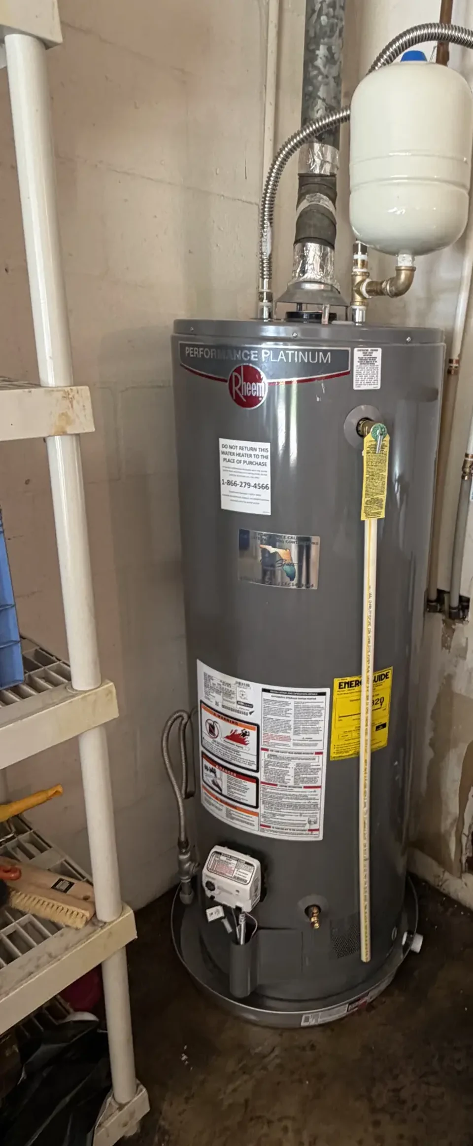 A gas tank water heater with overhead venting, supply connections, and an expansion tank.