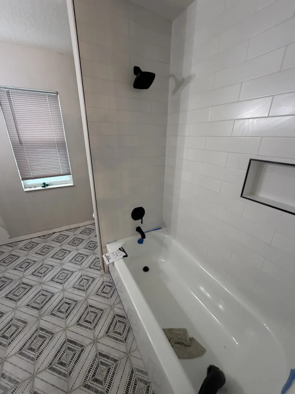 A bathtub and tiled shower with black showerhead, valve trim, and tub spout.