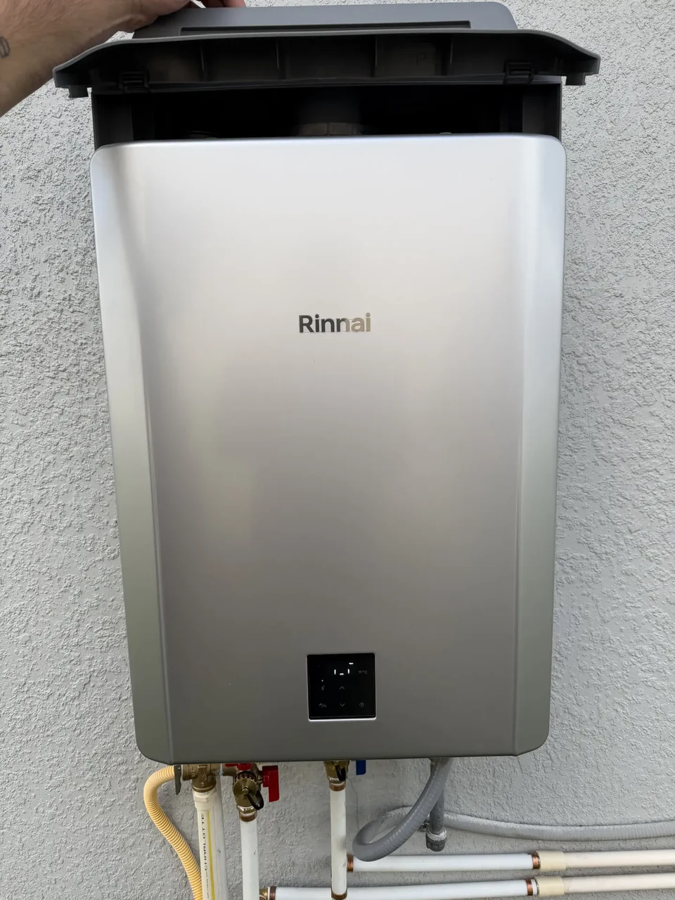 An outdoor Rinnai tankless water heater with connected supply lines and service valves.
