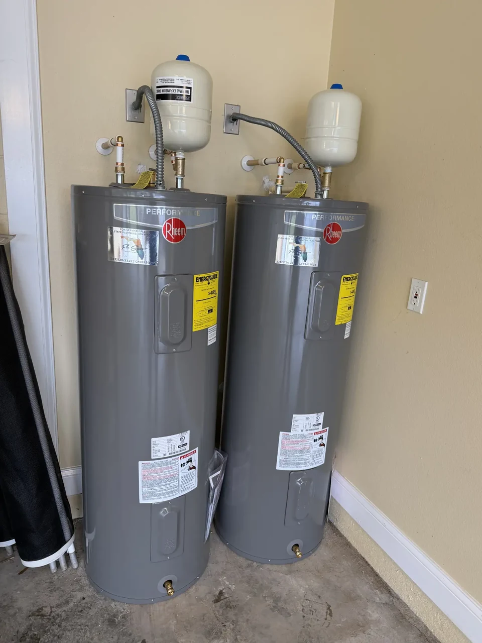 Two electric tank water heaters installed side by side, each with an expansion tank above.
