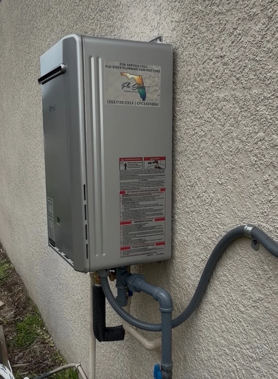 A wall-mounted tankless water heater with connected pipework outside a home.