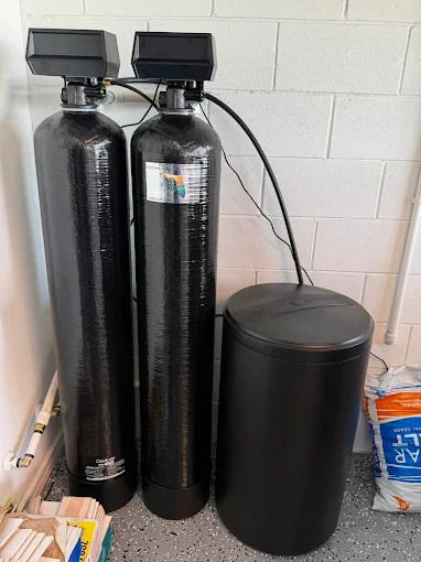 Two black softener tanks and a brine tank in a garage