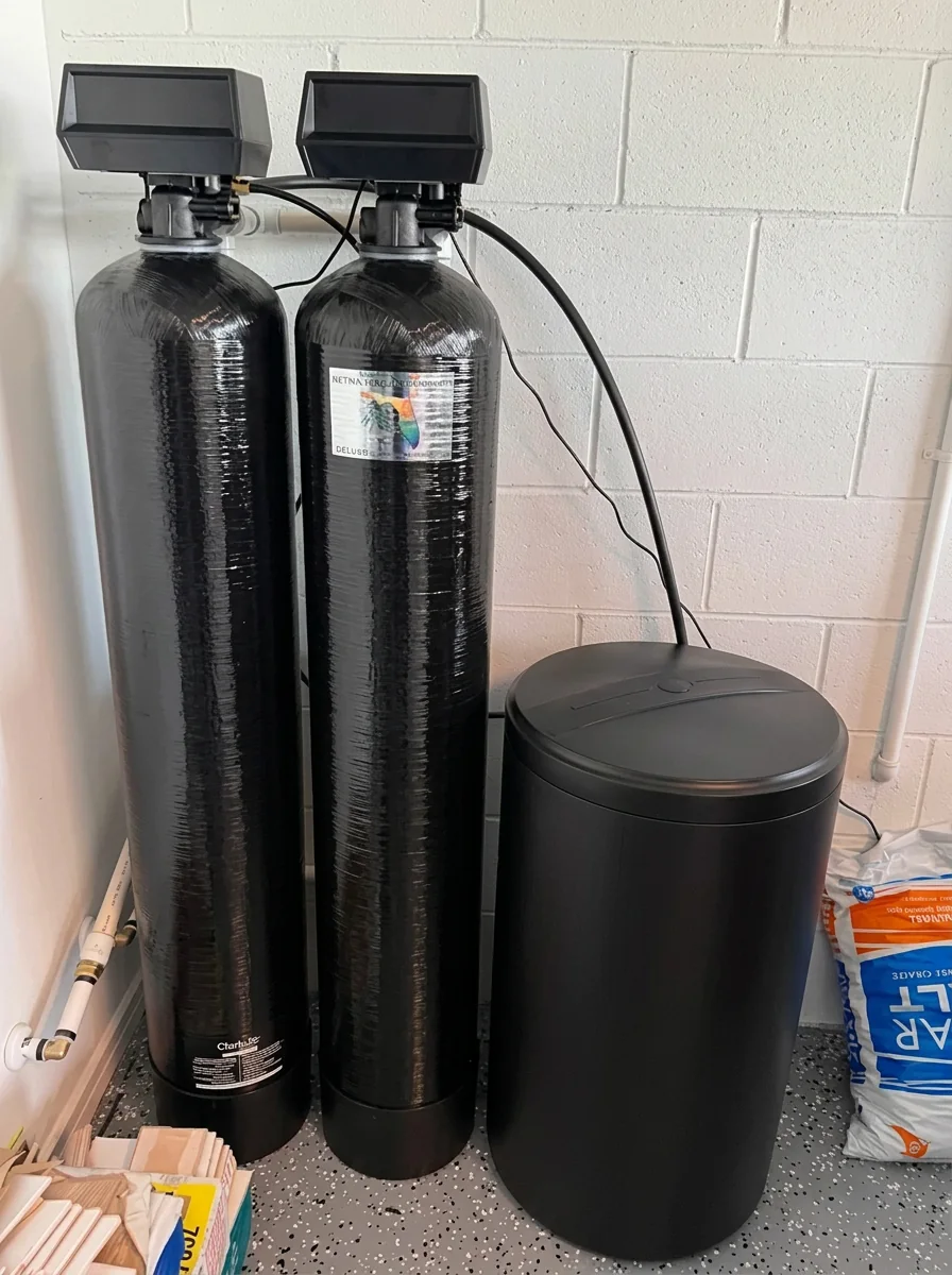 Two black softener tanks and a brine tank in a garage